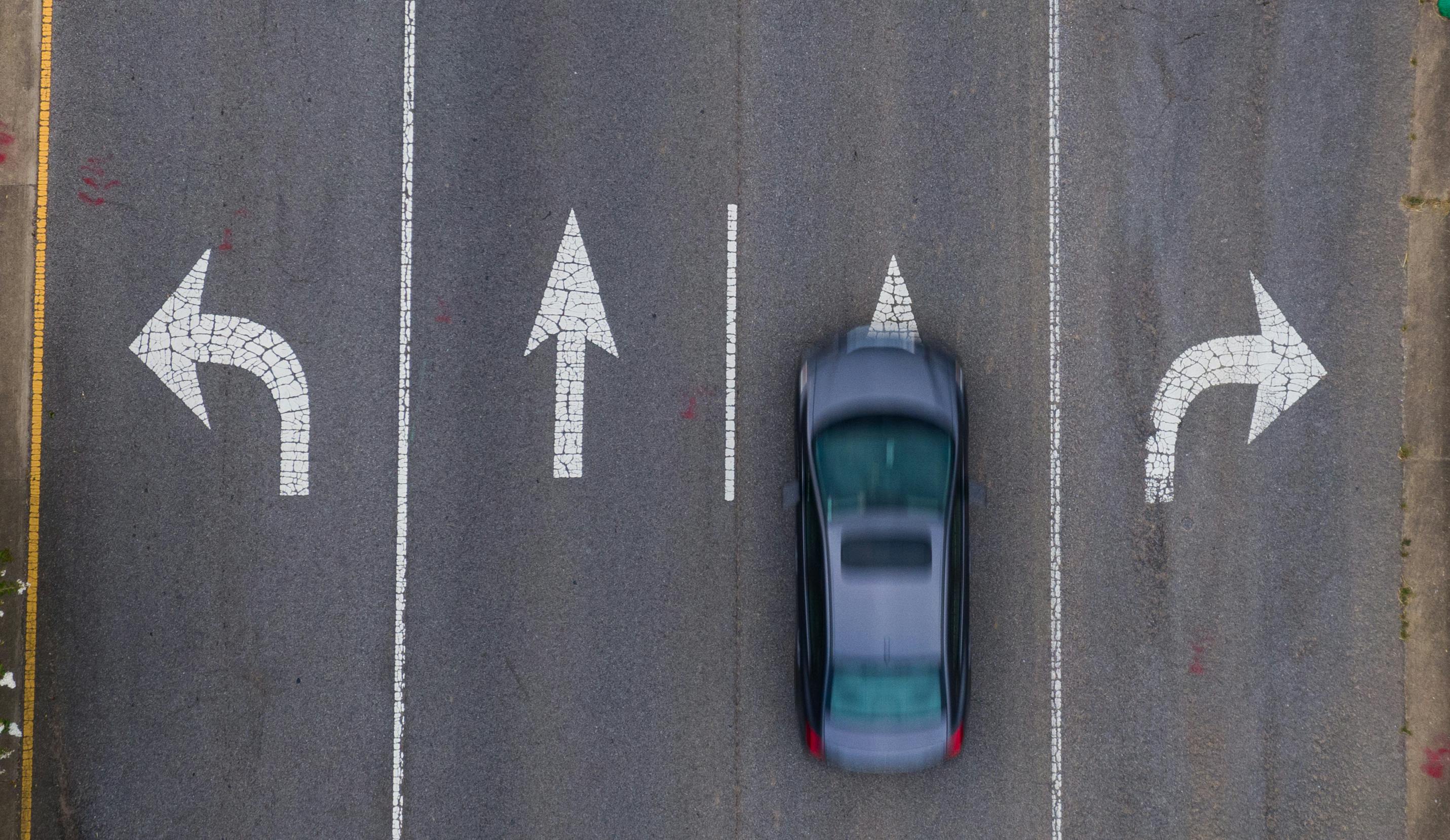 Aerial view of a four-lane road; left lane with a sign to turn left; right lane with a sign to turn right; middle lanes with signs to go straight